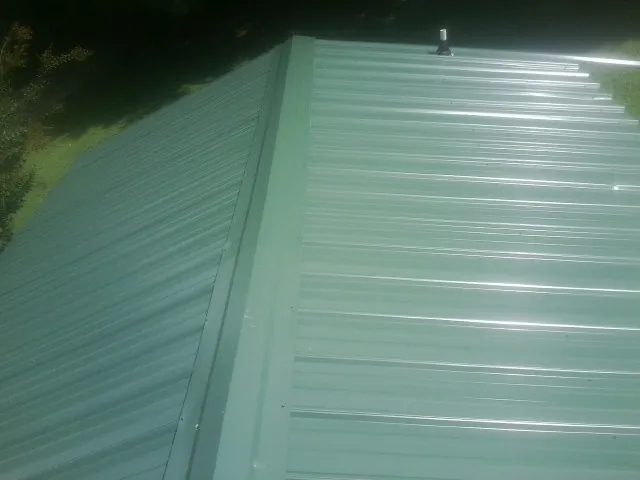 New green metal panels meeting at the ridge of a roof — Flat Roof Repair work by our crew in Colton